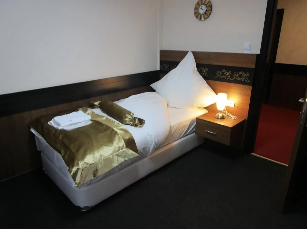 Einzelzimmer mit Einzelbett, goldener Tagesdecke und Nachttischlampe