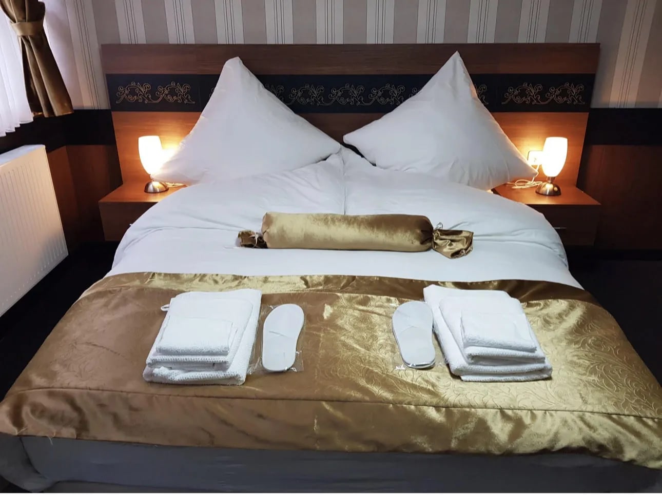 Doppelzimmer mit Doppelbett, goldener Tagesdecke, Handtüchern und Leselampen